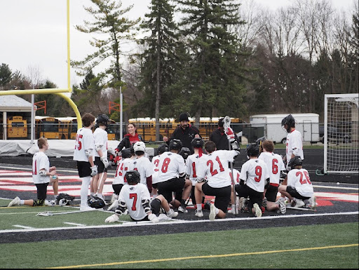 The boys lacrosse team has a team meeting on the field after a match.