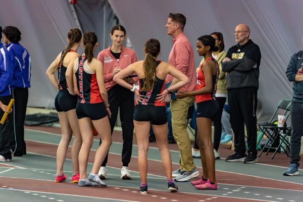 Girls track runners have pre-race meeting with distance coach Chad Wallace.