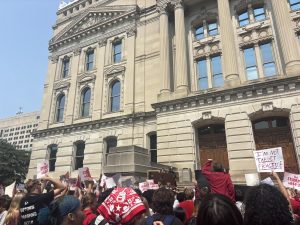 Students and adults hold signs and chant outside the state house to show their support for anti-gun violence speakers.
