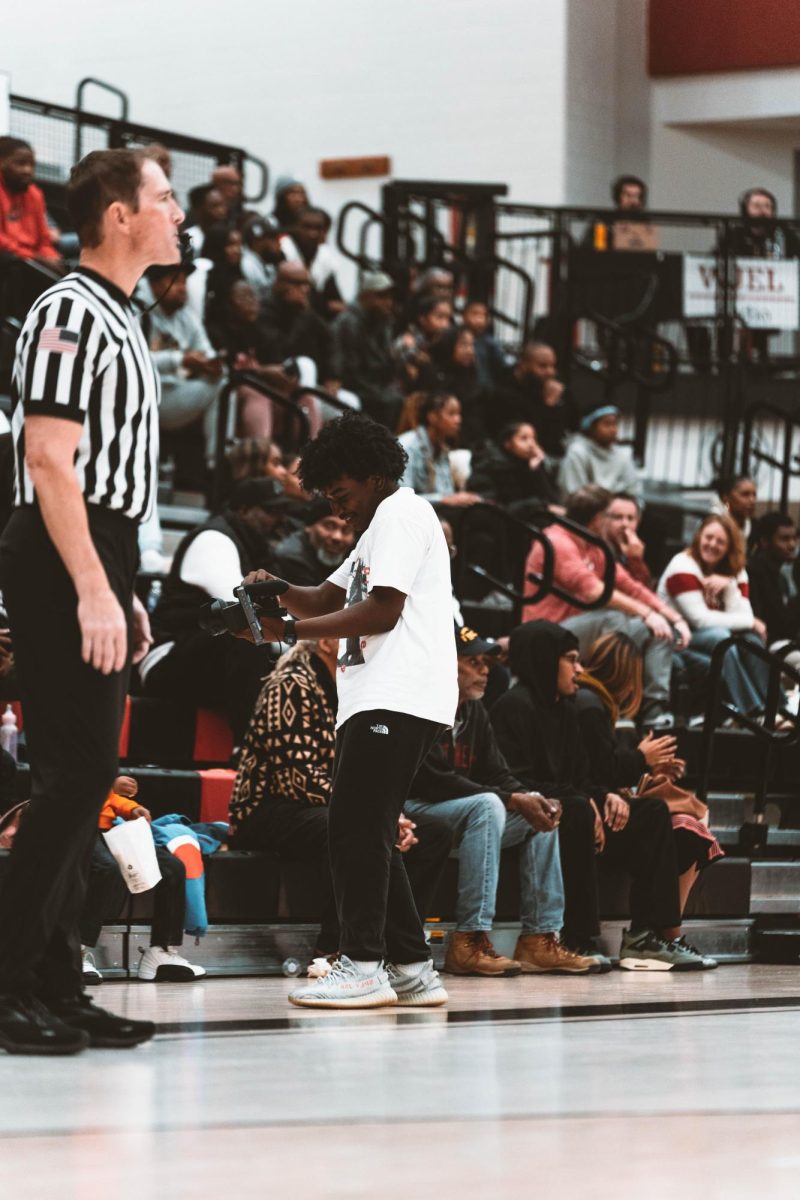 Junior Jayden Williams taking a video of fans cheering at boys basketball game.