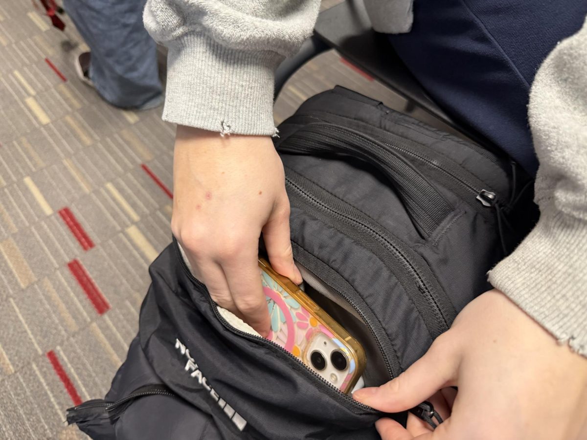 Junior Rose Strabala puts her phone into her backpack to prepare for class. “I think it is working but some people still have it (their phone) and get it taken,” said freshman Neve Bowden.